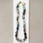Necklace with multicolored green, brown ad gray agate beads on a beige background
