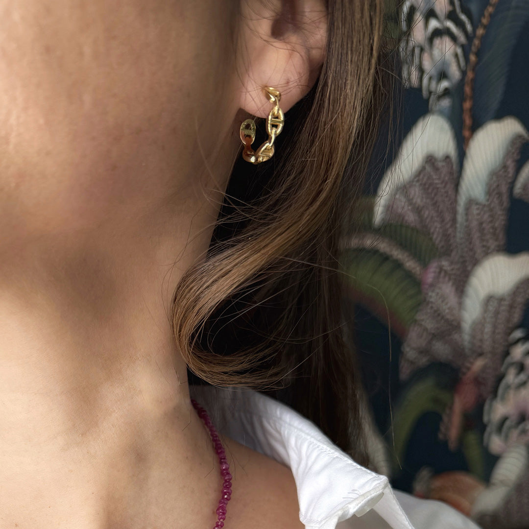 Gold chain link hoop earring worn by a person with dark hair.