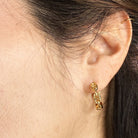 Gold chain link hoop earring worn by a person with dark hair.