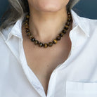 Woman wearing large Tigers Eye knotted gemstone necklace with a white shirt