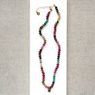 A smooth Watermelon Tourmaline beaded necklace in shades of pink, red, green, blue, and orange, featuring a small green tourmaline charm on a white card.