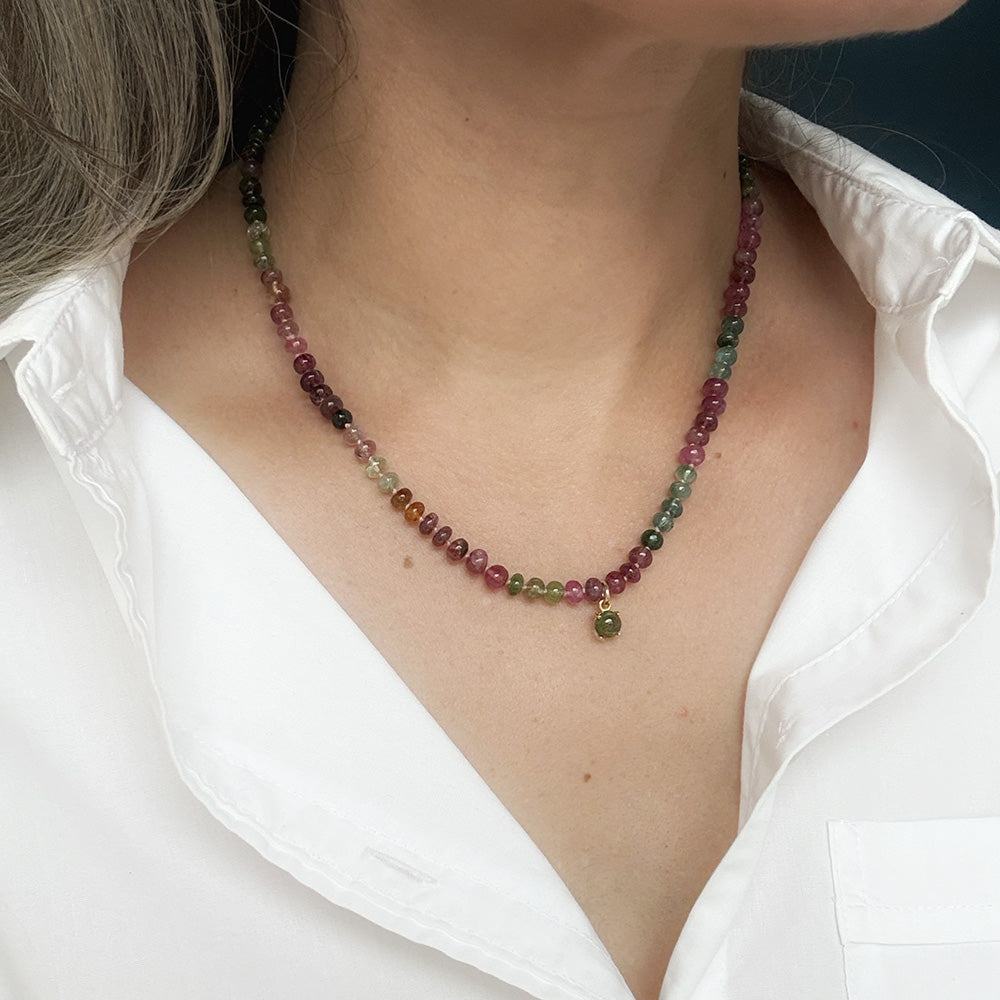 A close-up of a person wearing a smooth Watermelon Tourmaline necklace in shades of pink, red, green, blue, and orange, featuring a small green tourmaline charm, styled with a white collared shirt.