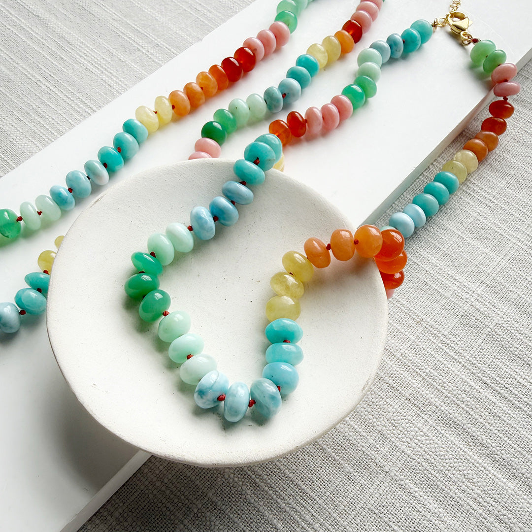 Colorful gemstone beaded necklaces on a white plate with a gray background