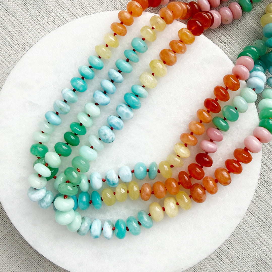 Colorful gemstone beaded necklaces on a white plate with a gray background