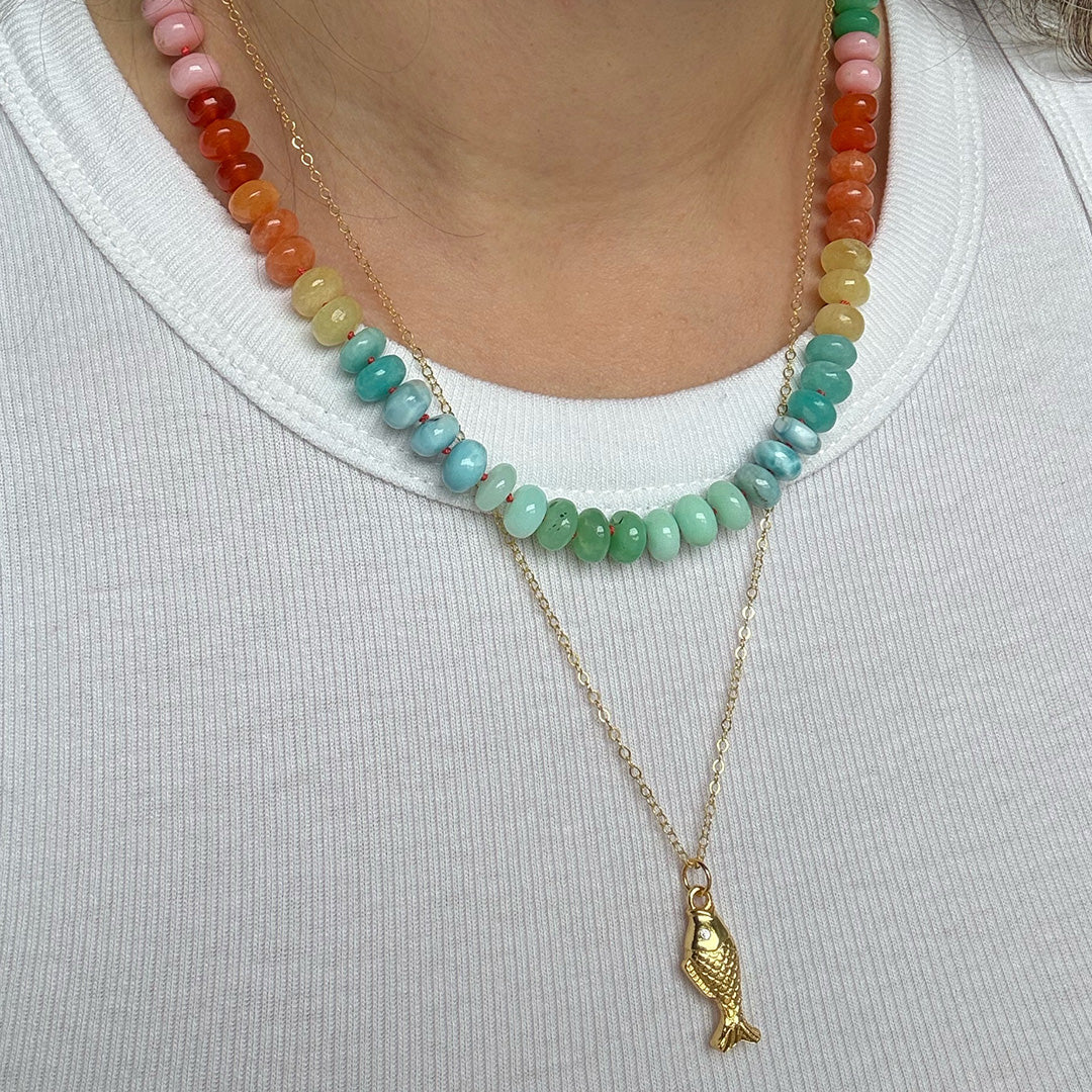 Colorful gemstone beaded necklace and gold fish pendant worn by a person with a white tank top
