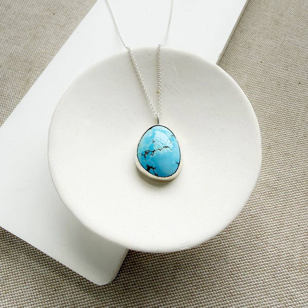 Golden Hills turquoise pendant necklace in sterling silver in a white dish.