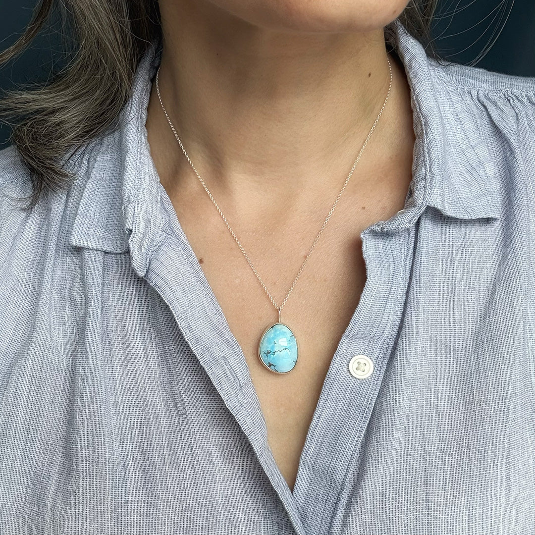 Person wearing a light blue shirt with a Golden Hills turquoise pendant necklace.
