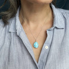 Person wearing a light blue shirt with a Golden Hills turquoise pendant necklace.