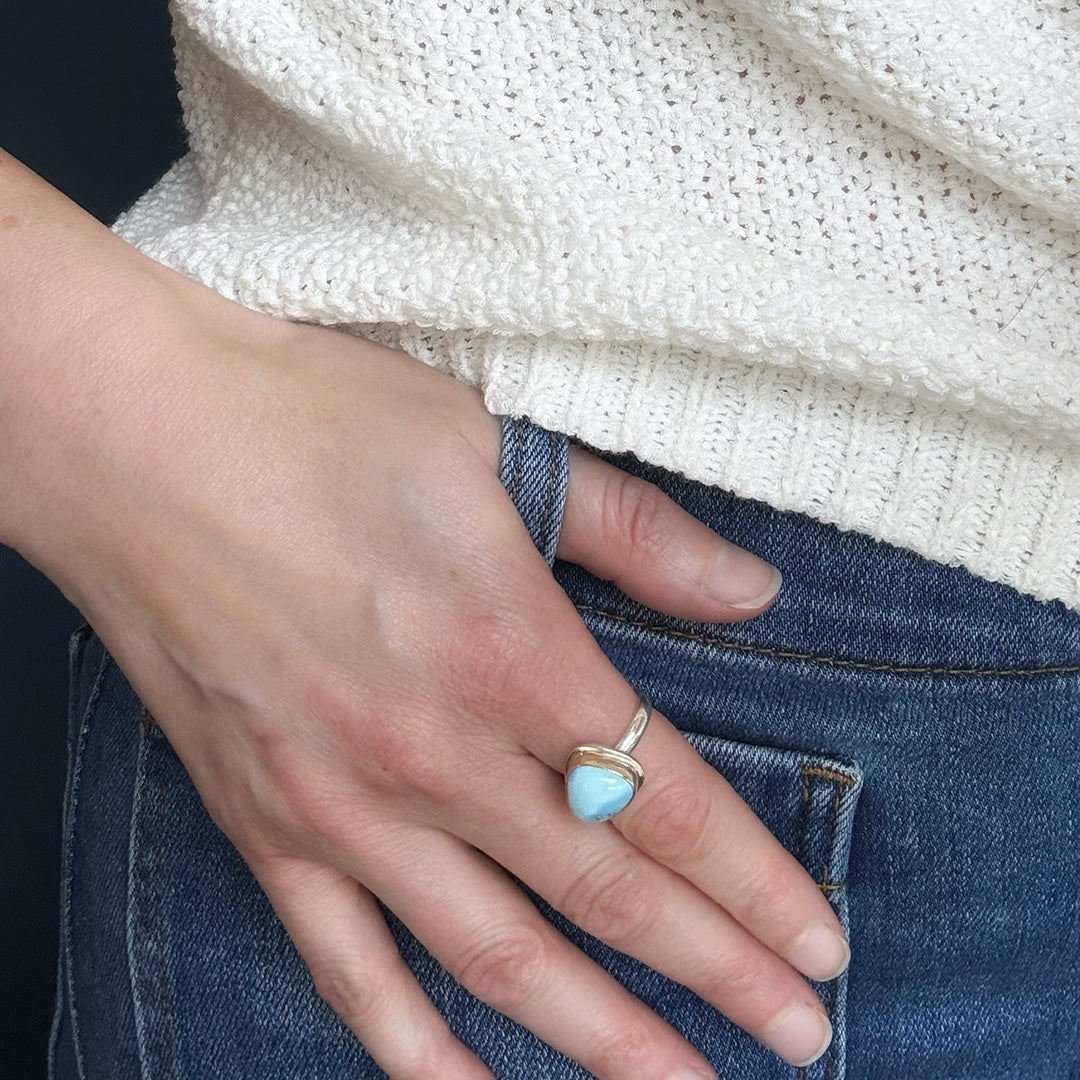 Hand wearing a one of a kind Golden Hills turquoise ring on a white sweater and blue jeans background