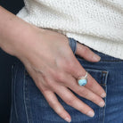 Hand wearing a Golden Hills turquoise silver ring on a dark background