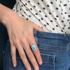 Hand wearing a Golden Hills turquoise ring in silver, against a dark background.
