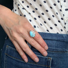 Hand wearing a Golden Hills turquoise ring with a polka dot shirt and blue jeans in the background