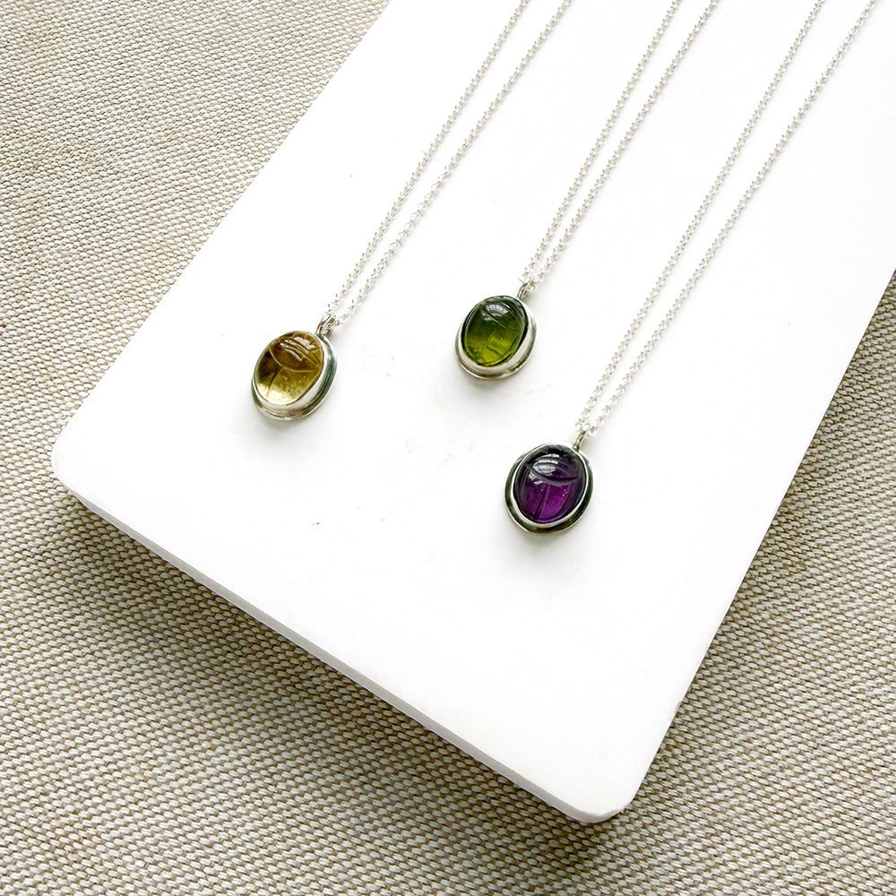 Three gemstone pendants with carved details on a white plate