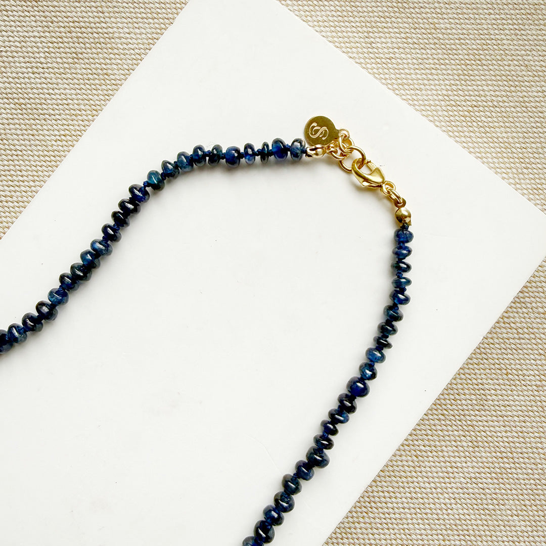 Necklace with blue sapphire gems and gold clasp on a white card