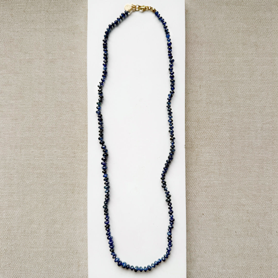 Knotted necklace with smooth sapphire gemstones on a white plate