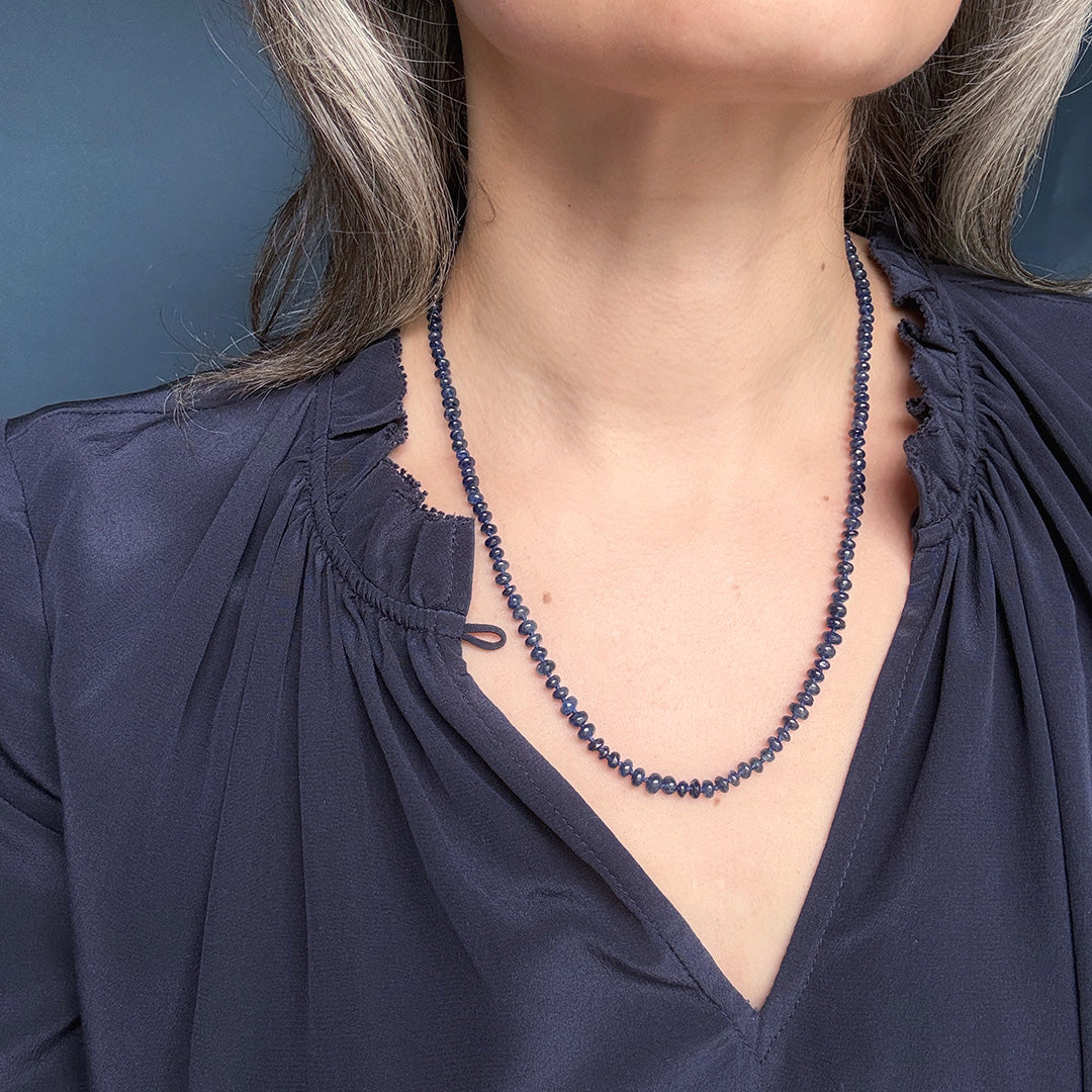 Person wearing a blue sapphire gemstone necklace against a dark background