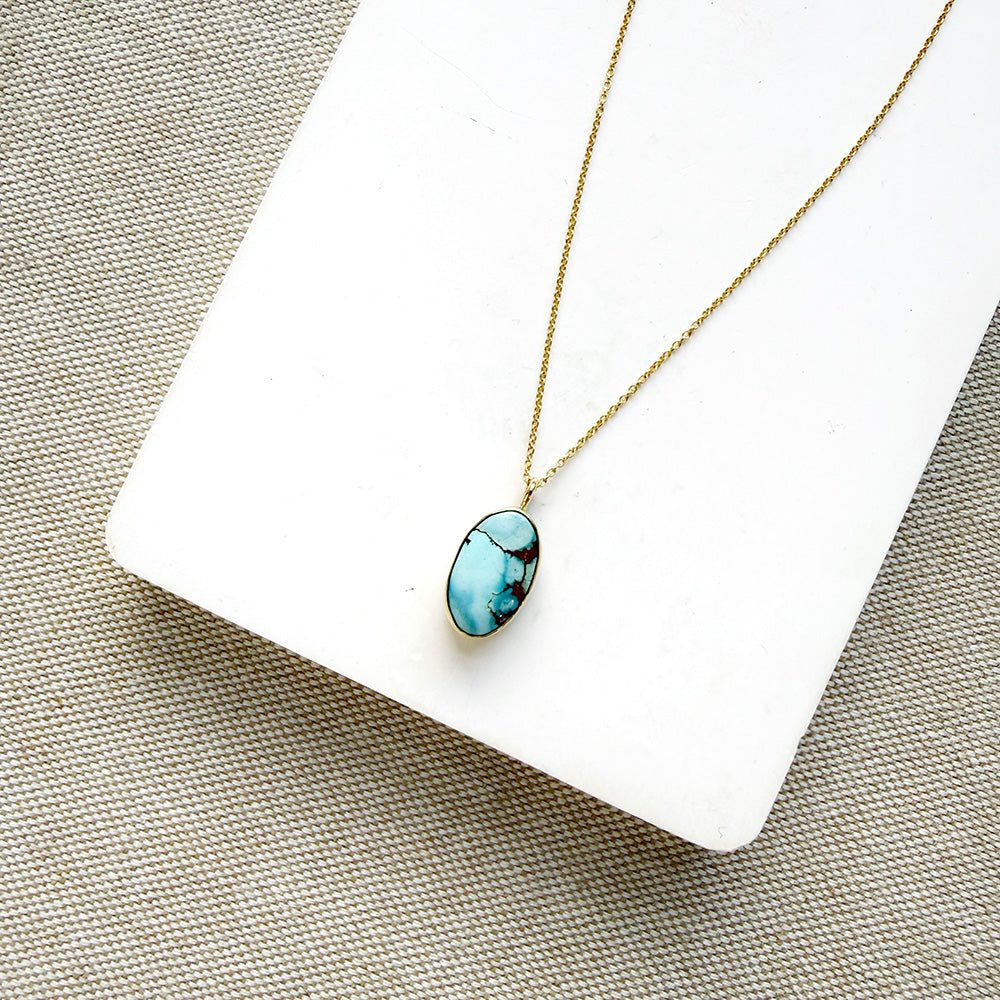 Small oval Golden Hills Pendant set in solid gold on a white plate