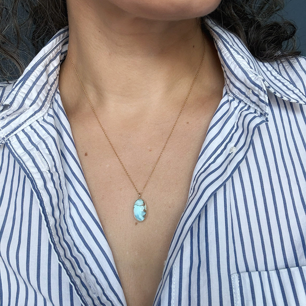 Woman wearing mall oval Golden Hills Pendant set in solid gold with a striped shirt