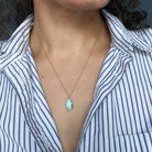 Woman wearing mall oval Golden Hills Pendant set in solid gold with a striped shirt