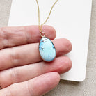 Golden Hills turquoise pendant necklace held between fingers on a neutral background