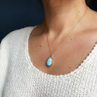 A Golden Hills turquoise pendant necklace worn by a person in a white textured top against a dark background