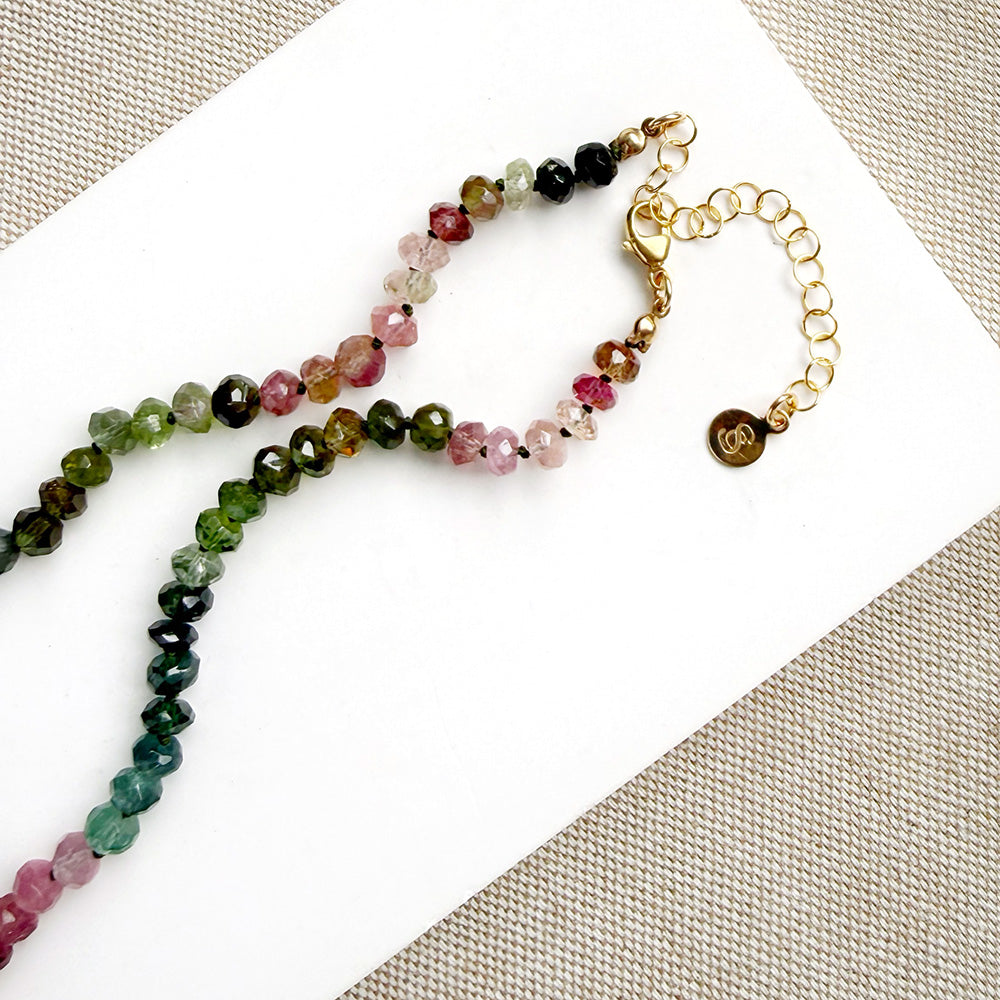 Clasp detail of a beaded necklace made of Watermelon Tourmaline faceted round beads in shades of green, blue, and pink, on a textured beige fabric background.