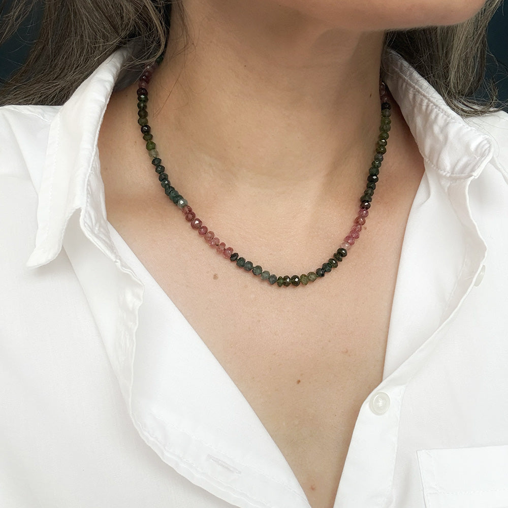 A close-up of a person wearing a necklace made of Watermelon Tourmaline faceted beads, paired with a white collared shirt.