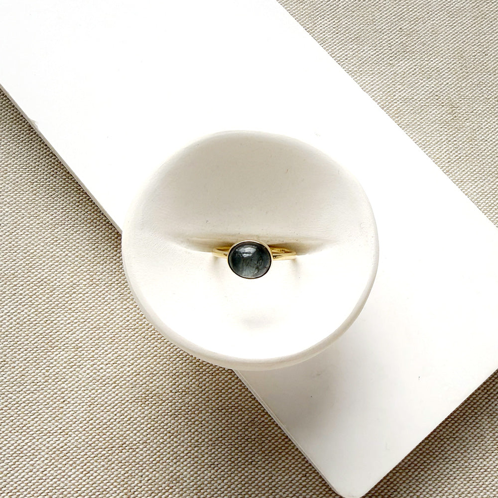Grey spinel and solid gold ring on a white dish