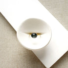 Grey spinel and solid gold ring on a white dish