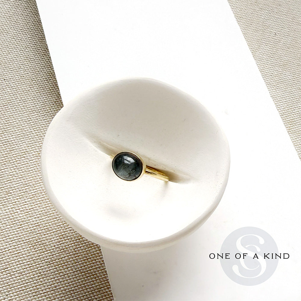 Grey spinel and solid gold ring in a white dish