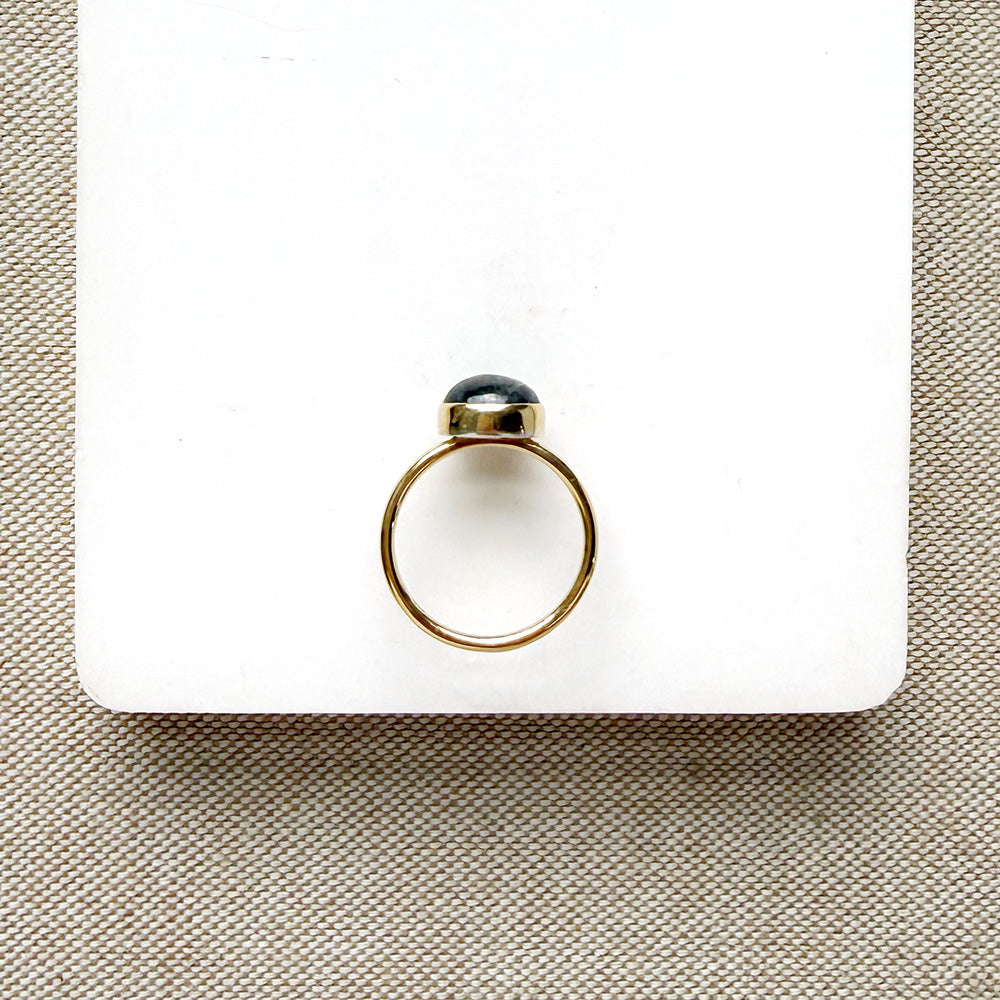 Grey spinel and solid gold ring on a white dish