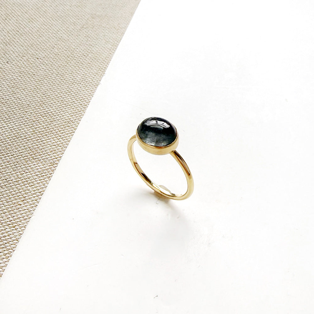 Grey spinel and solid gold ring on a white dish