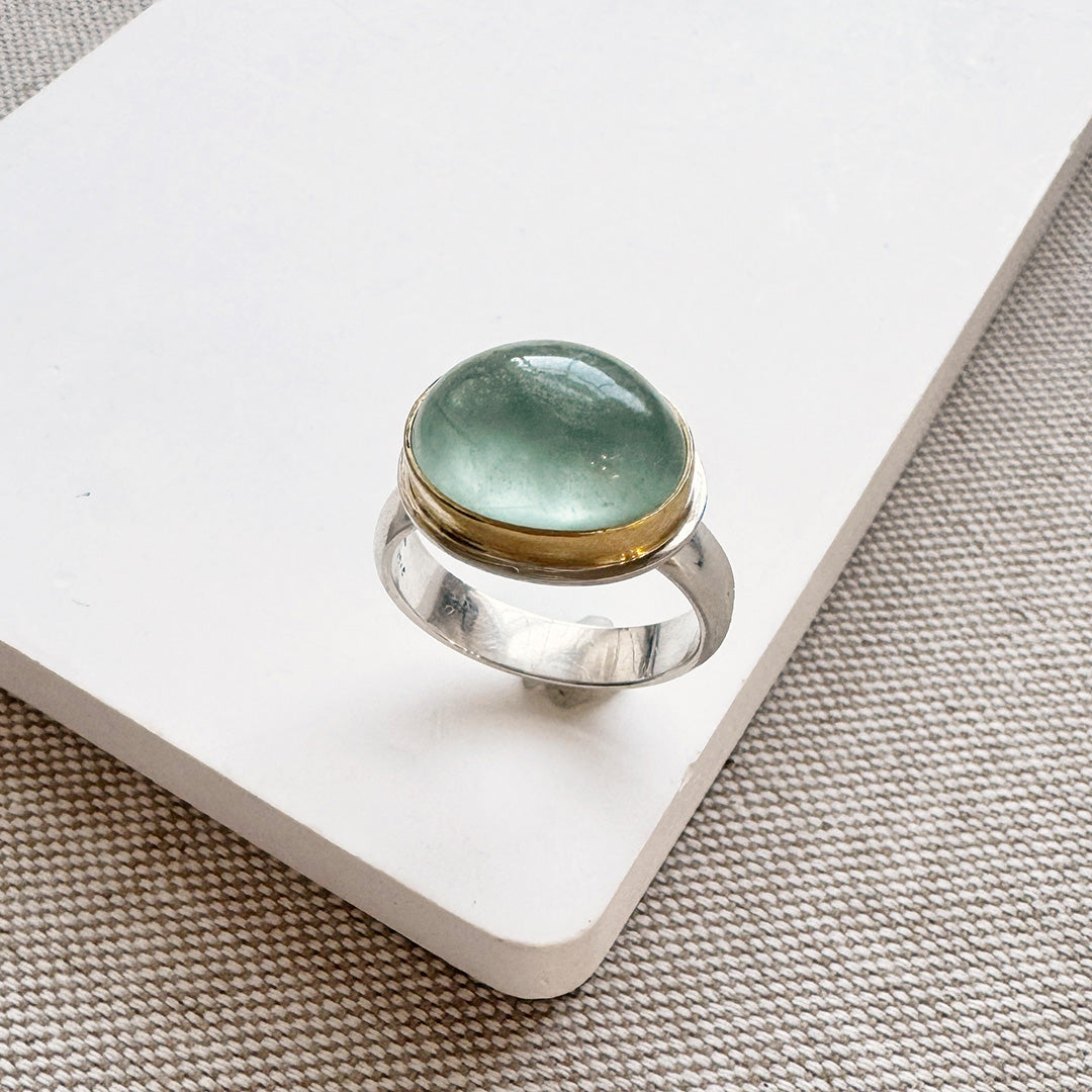 Ring with a green aquamarine stone on a white card with a textured beige background