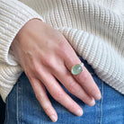 Hand wearing a ring with a green aquamarine stone against a neutral background