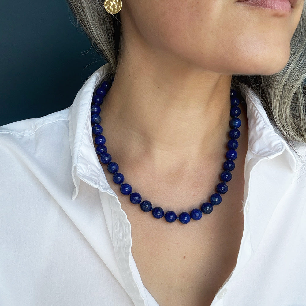 A close-up of a woman wearing a dark blue lapis lazuli necklace, styled with a white collared shirt.
