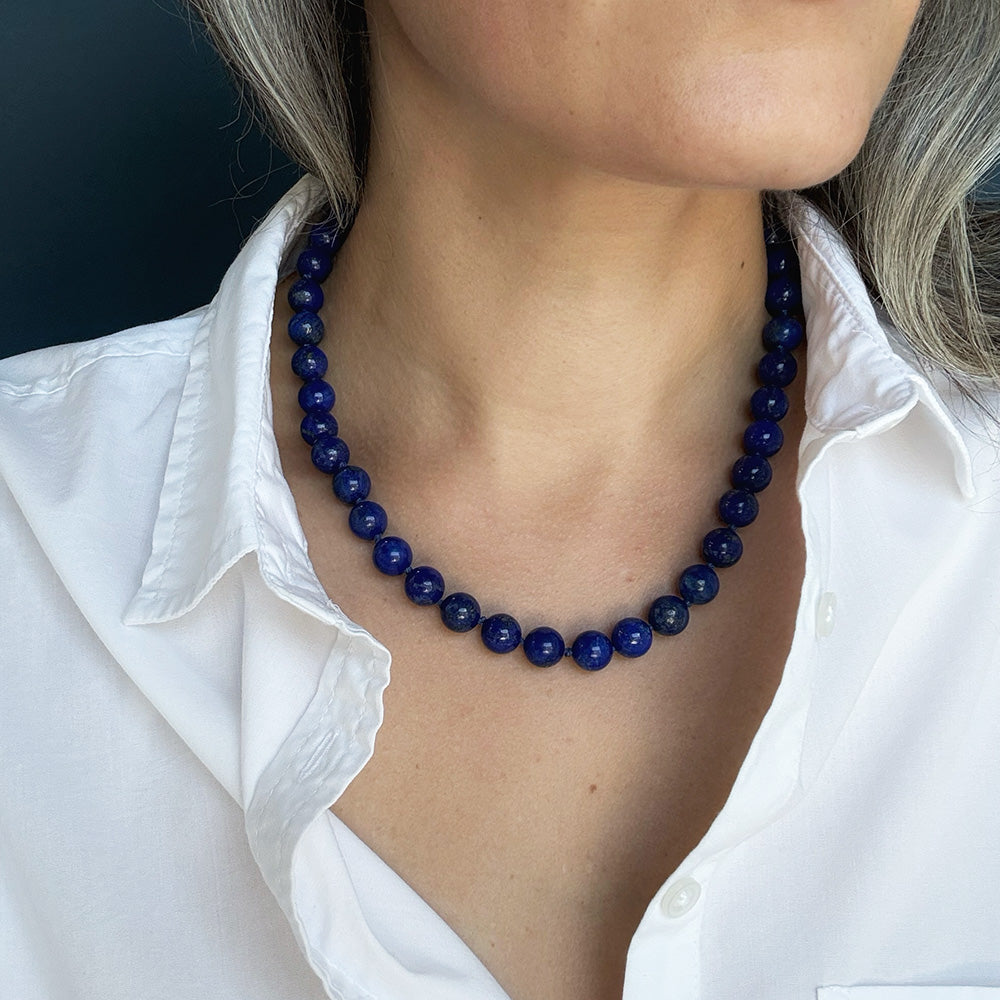 A close-up of a woman wearing a dark blue lapis lazuli necklace, styled with a white collared shirt.