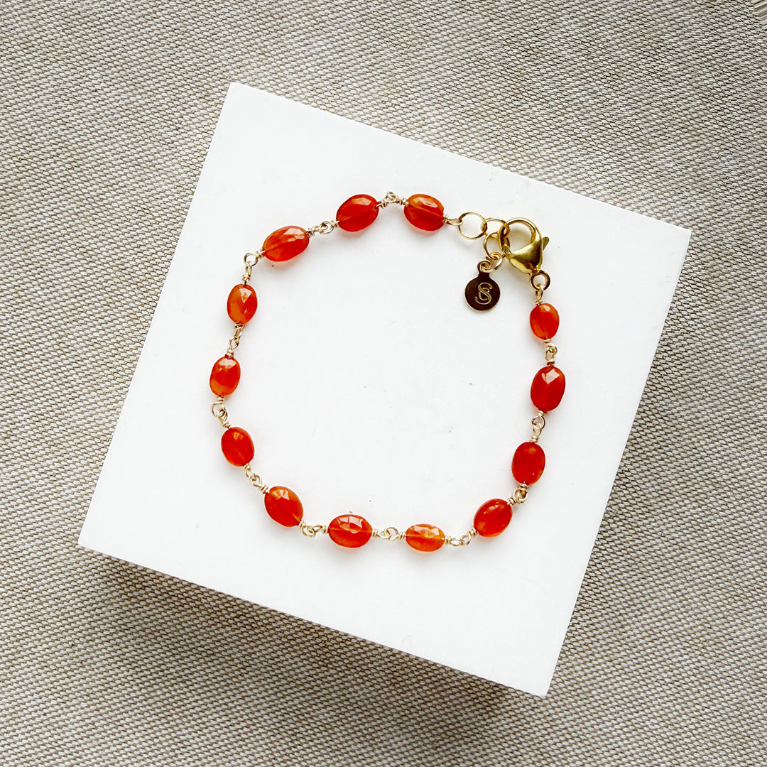 Bracelet with carnelian gemstones on a white card against a textured gray background