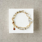 Gold bracelet with blue and clear gemstones on a white card against a beige fabric background