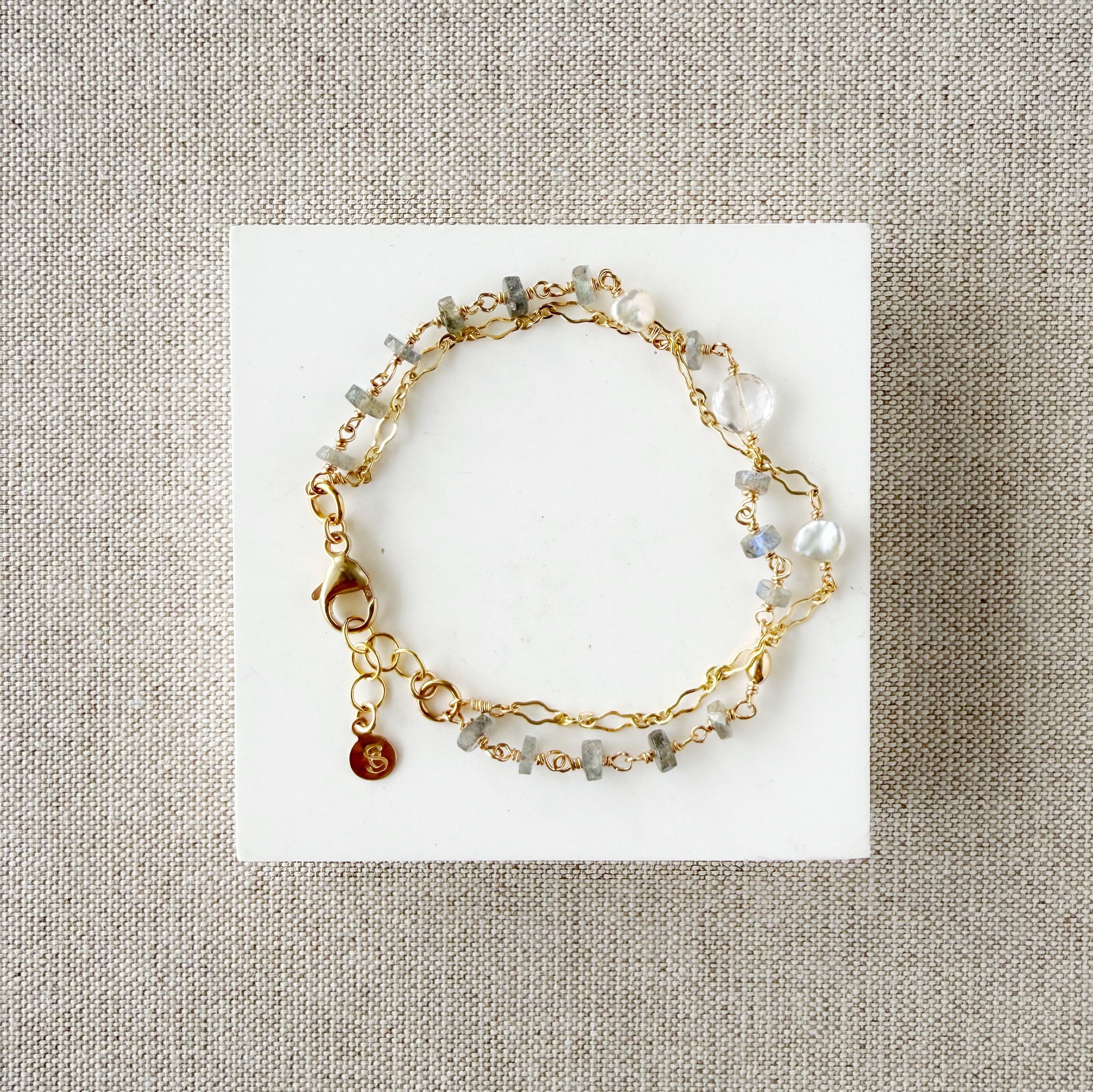 Gold bracelet with blue and clear gemstones on a white card against a beige fabric background