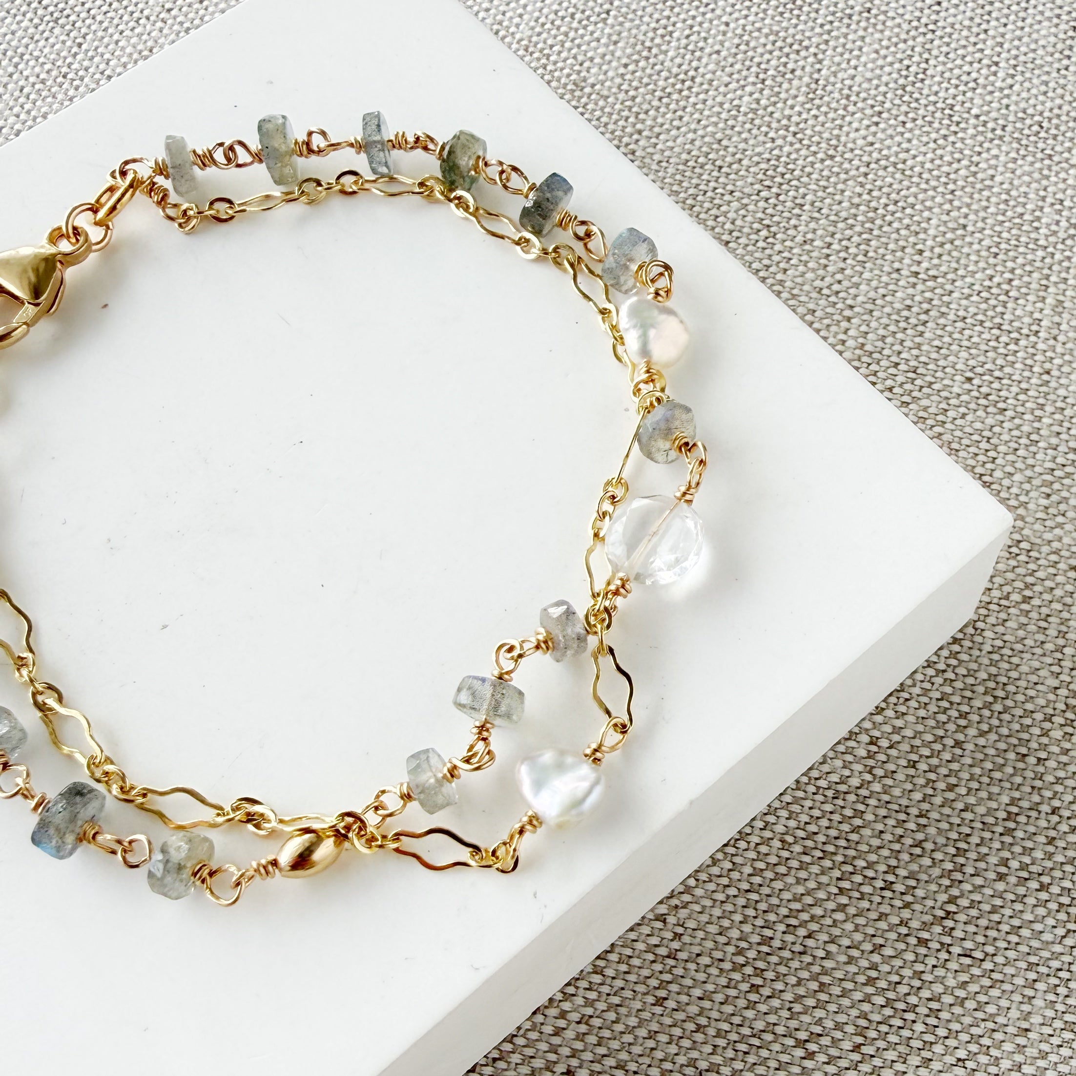 Gold bracelet with blue and clear gemstones on a white card against a beige fabric background