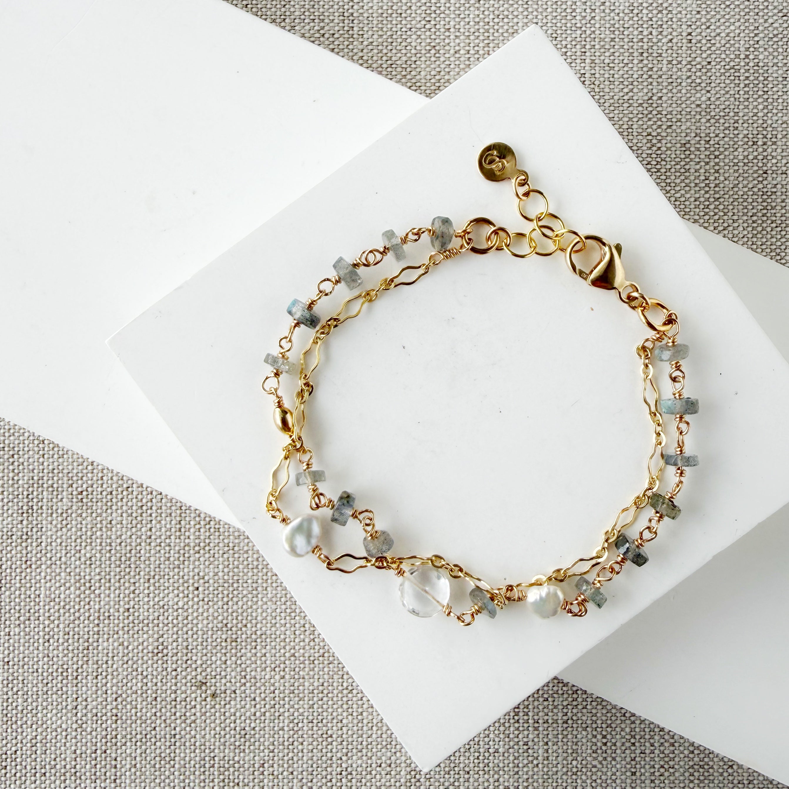 Gold bracelet with blue and clear gemstones on a white card against a beige fabric background