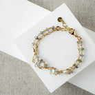 Gold bracelet with blue and clear gemstones on a white card against a beige fabric background