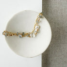 Gold bracelet with blue and clear gemstones on a white card against a beige fabric background