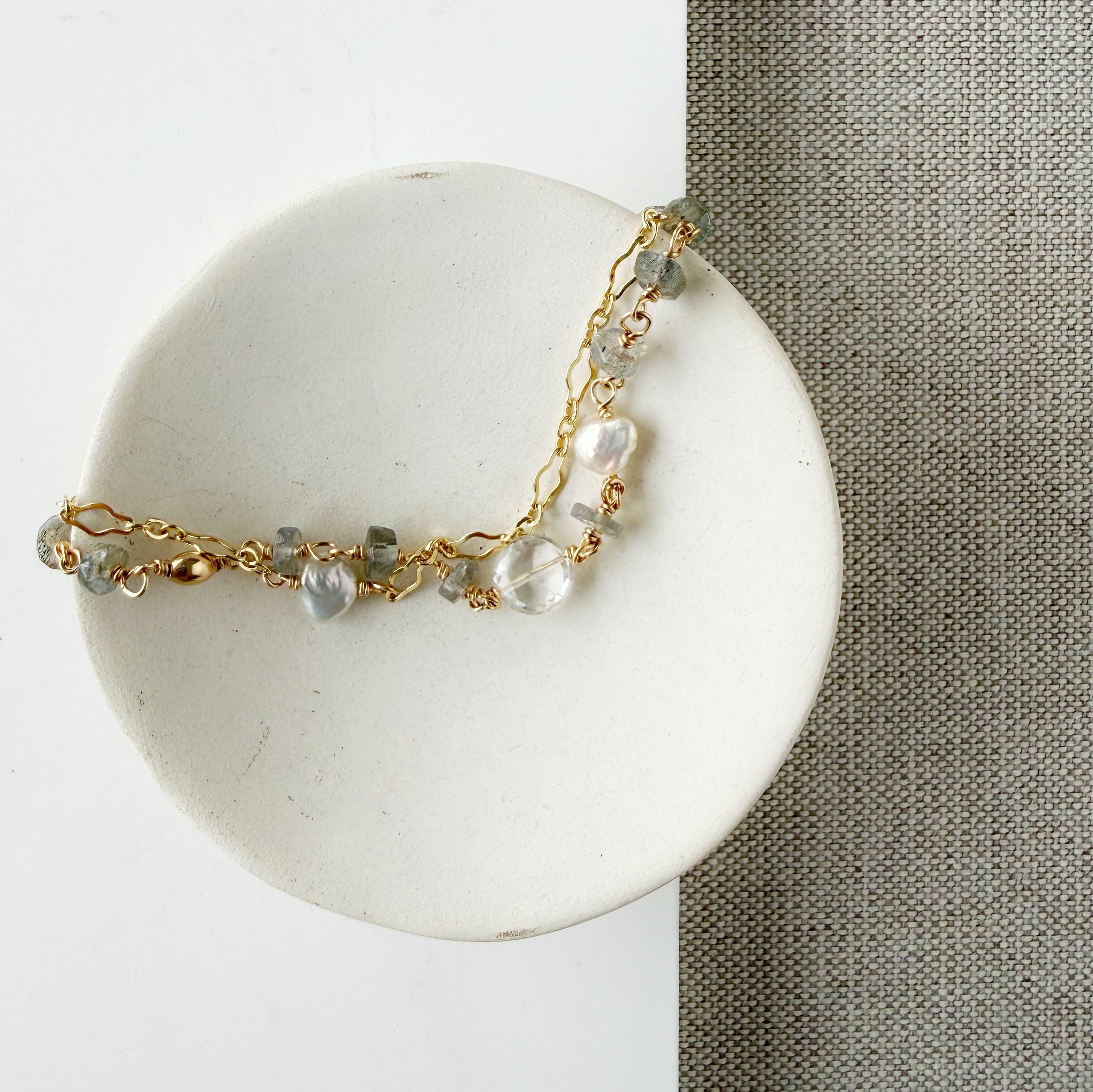 Gold bracelet with blue and clear gemstones on a white card against a beige fabric background