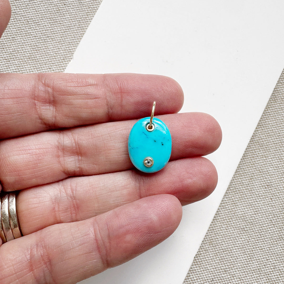 Hand holding an oval blue howlite charm with inset quartz stone