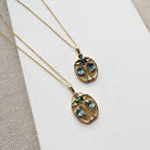 Two gold beetle-shaped pendant necklaces with blue gemstones, displayed on a white card over a textured beige fabric background.