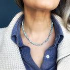 Person wearing a Golden Hills Turquoise beaded necklace with a blue shirt and beige jacket against a dark background