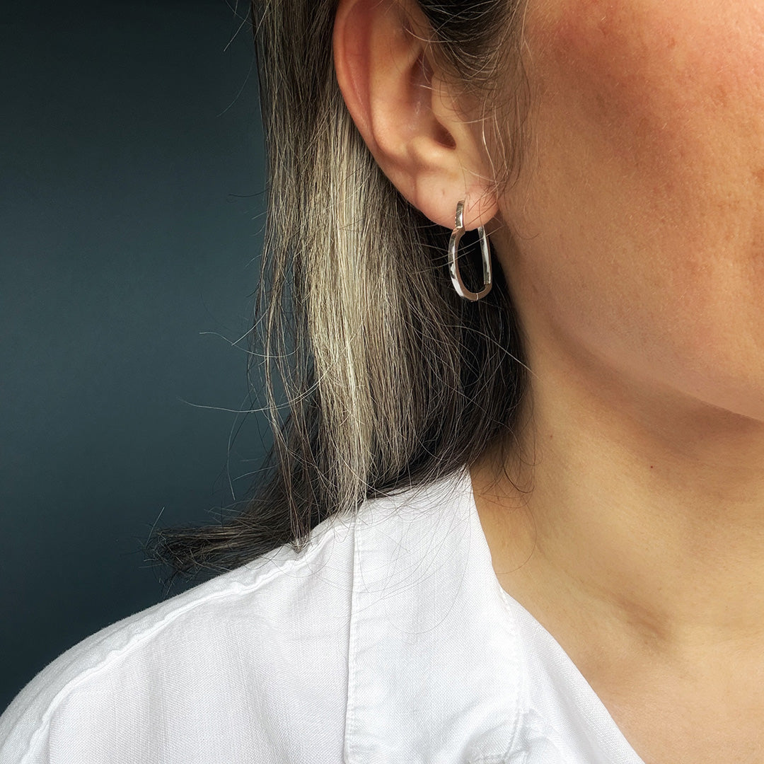 Close-up of an ear wearing a silver heart hoop earring with a dark background