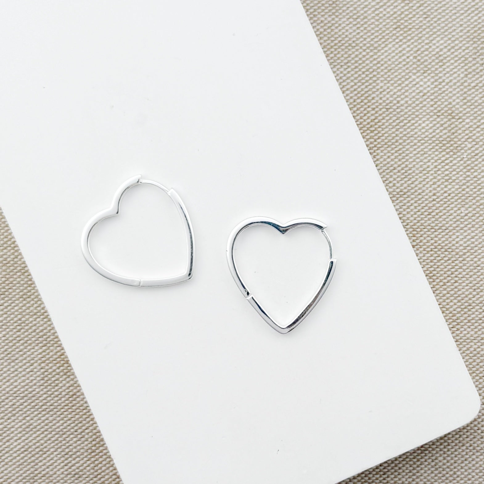 Heart-shaped silver hoops on a white card with a beige background