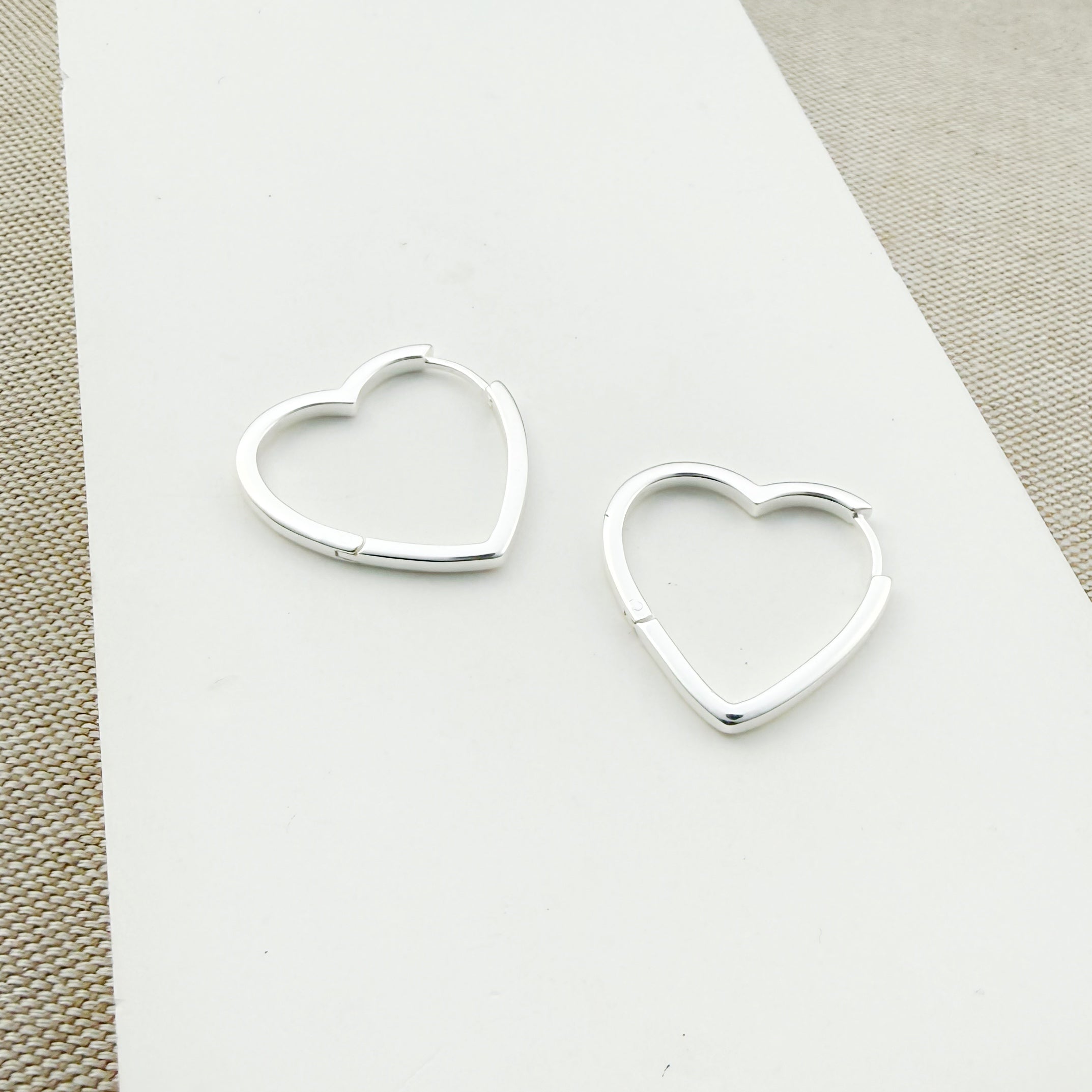 Heart-shaped silver hoops on a white card with a beige background